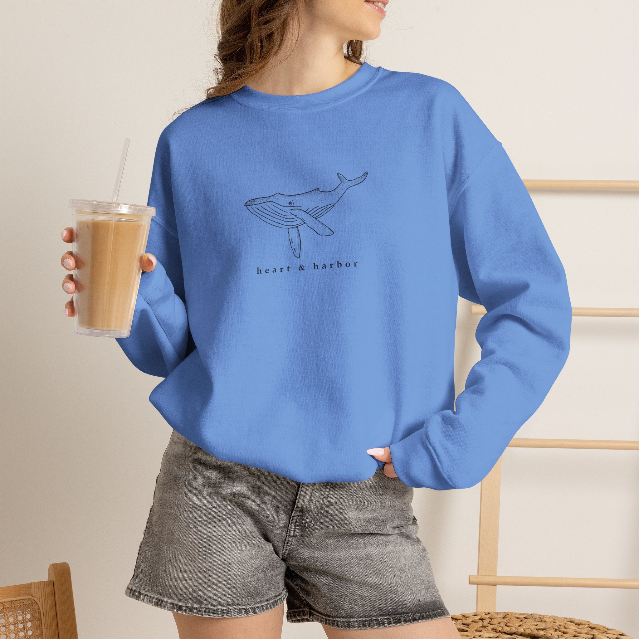 Person wearing a blue hand-drawn whale crewneck sweatshirt by Heart & Harbor