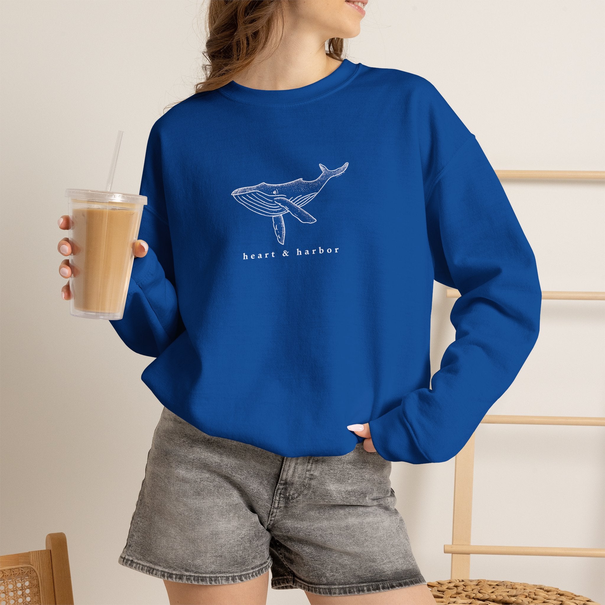 Person wearing a navy hand-drawn whale crewneck sweatshirt by Heart & Harbor