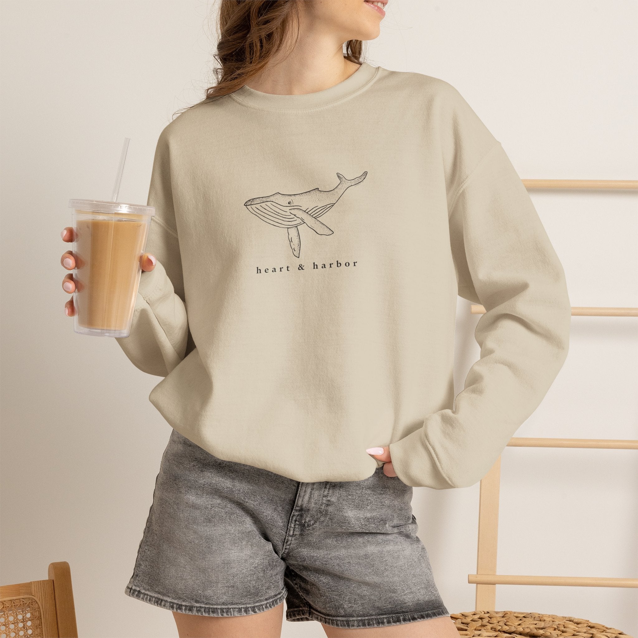 Person wearing a sand hand-drawn whale crewneck sweatshirt by Heart & Harbor