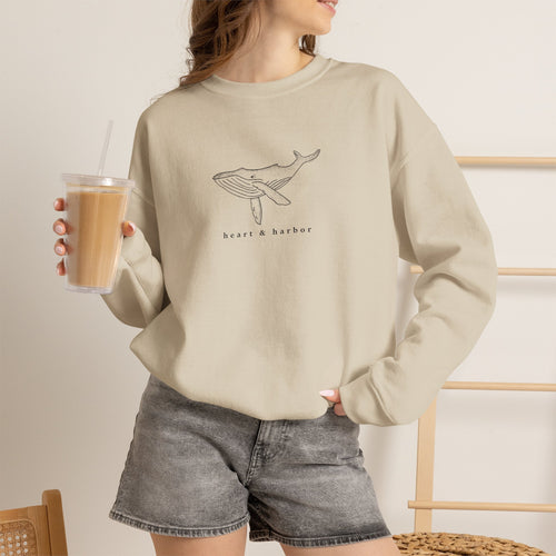 Person wearing a sand hand-drawn whale crewneck sweatshirt by Heart & Harbor
