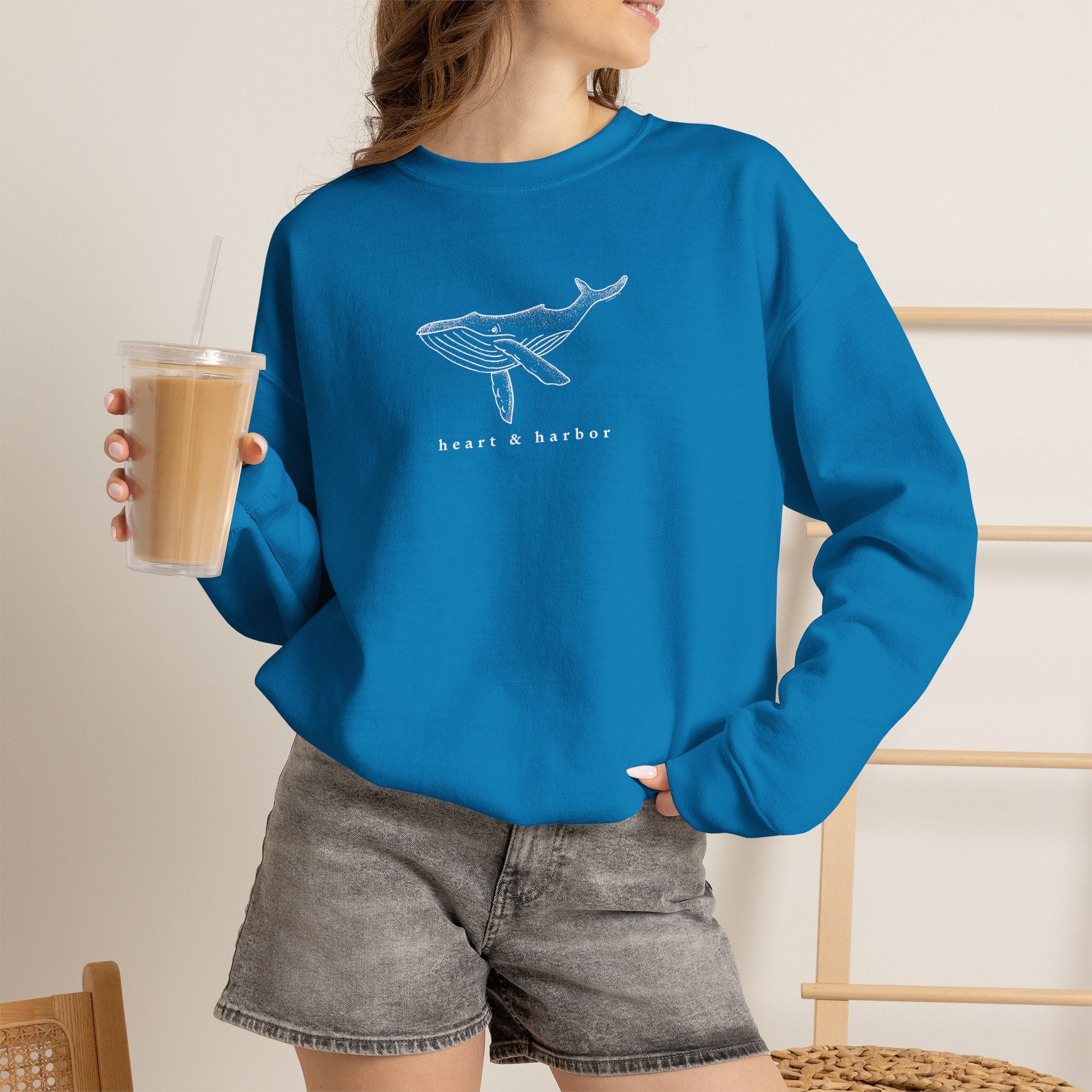 Person wearing a saphire hand-drawn whale crewneck sweatshirt by Heart & Harbor