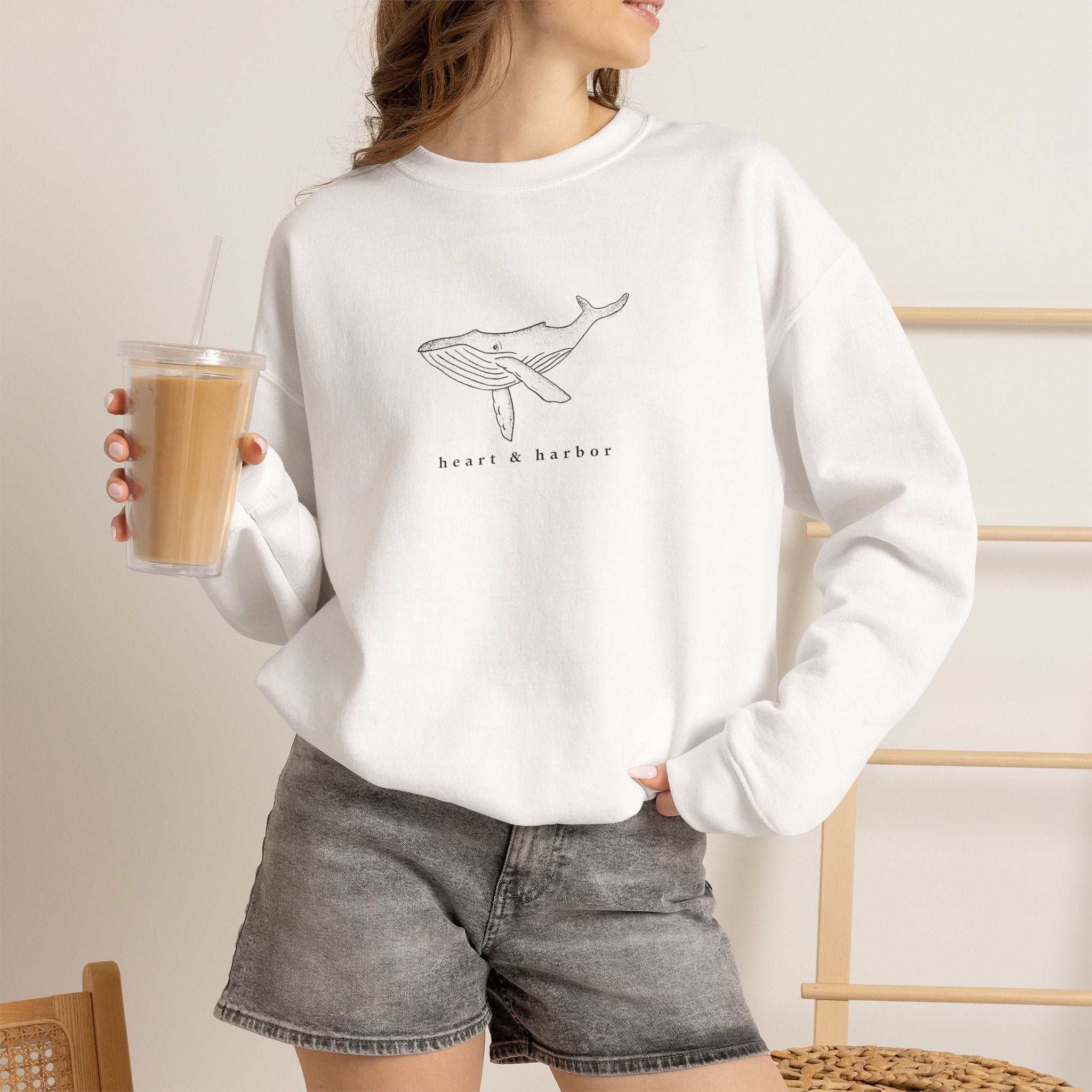 Person wearing a white hand-drawn whale crewneck sweatshirt by Heart & Harbor