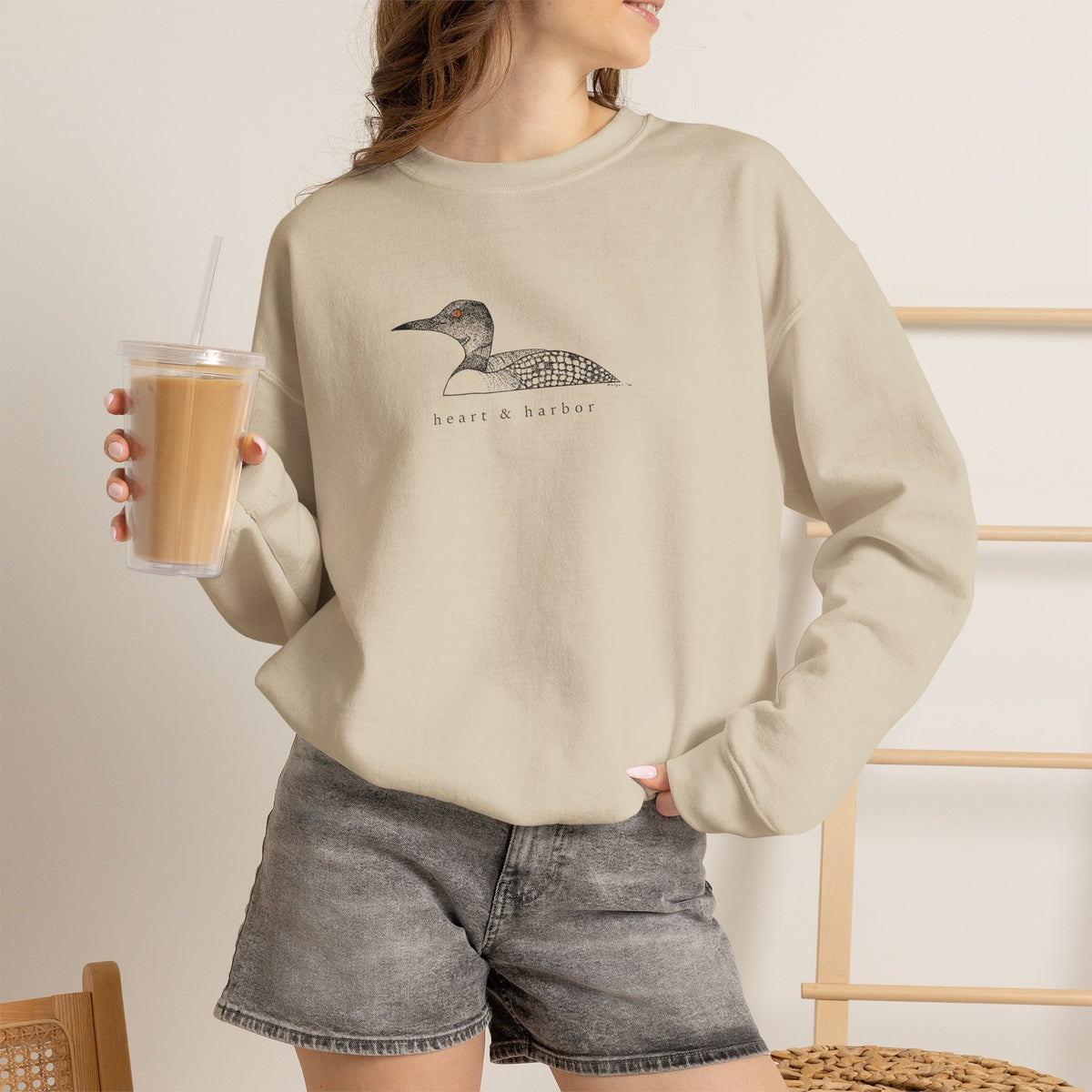 Unisex tan Gildan 18000 crewneck sweatshirt featuring original hand-drawn Heart & Harbor common loon artwork